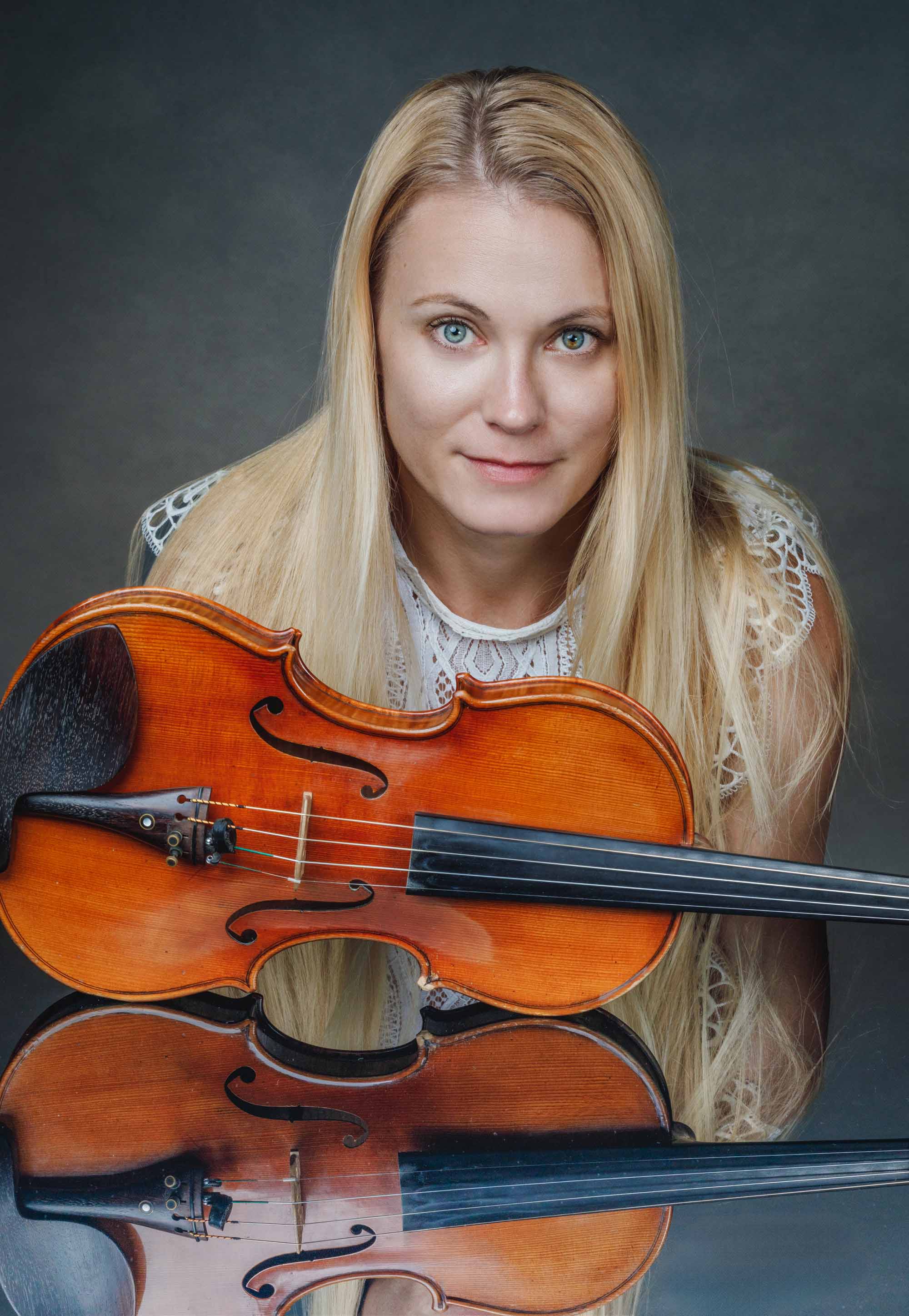 blonde Geigerin und ihre Geige spiegeln sich auf einer schwarzen Fläche